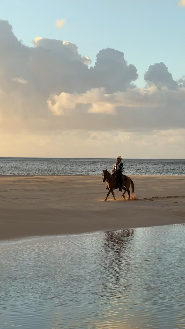 A rider crossing wet sand at sunrise
