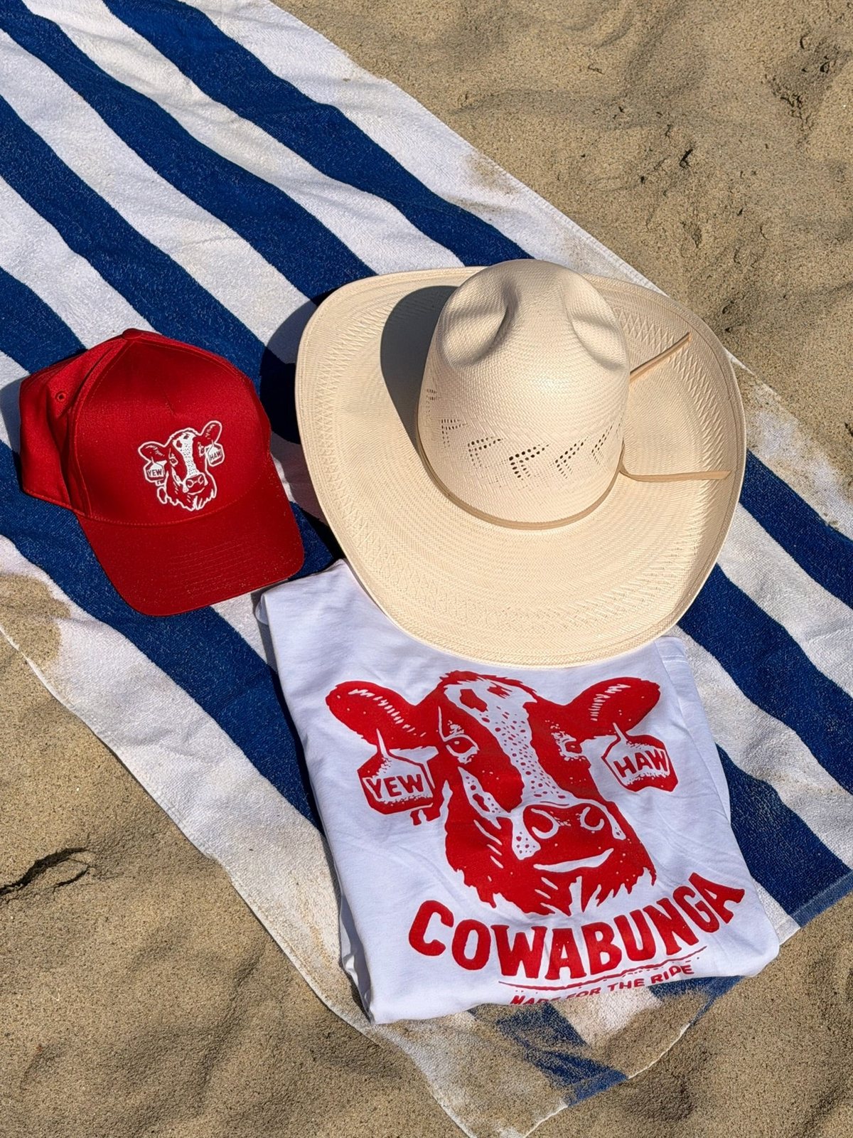 The Yewhaw cap on a striped beach towel next to a straw cowboy hat