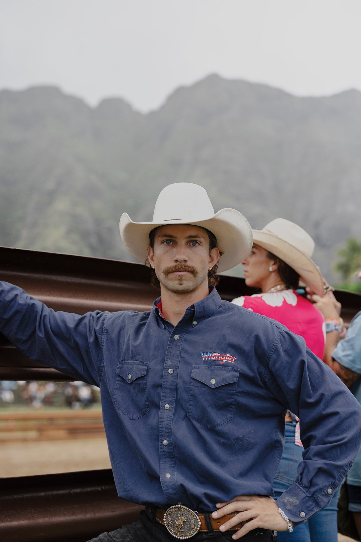 Mitch Mayes in a straw cowboy hat at a rodeo, the Koʻolau range behind him